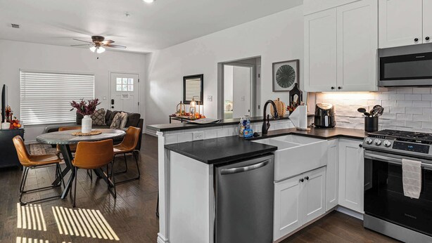 A modern kitchen with white cabinets, a black countertop, stainless steel appliances, and a dining area with a round table and chairs. - Homestead - Close to Main St & 290 Wine Trail (Fredericksburg)