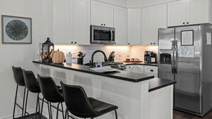 A modern kitchen with white cabinets, a stainless steel refrigerator, a microwave, and a coffee station. - Homestead - Close to Main St & 290 Wine Trail (Fredericksburg)