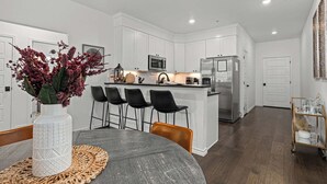 A modern kitchen with white cabinetry, a central island with bar stools, and a dining area with a round table and chairs. - Homestead - Close to Main St & 290 Wine Trail (Fredericksburg)