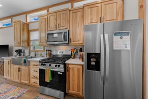 A kitchen with wooden cabinets, a stainless steel refrigerator, a microwave, a stove, and a water dispenser.