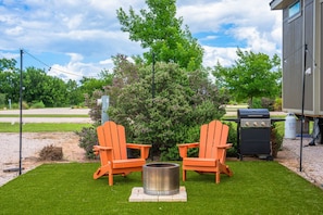 A patio with two orange Adirondack chairs, a metal fire pit, and a grill.