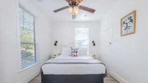 A bedroom with a bed, ceiling fan, bedside lamps, and a window with blinds.
