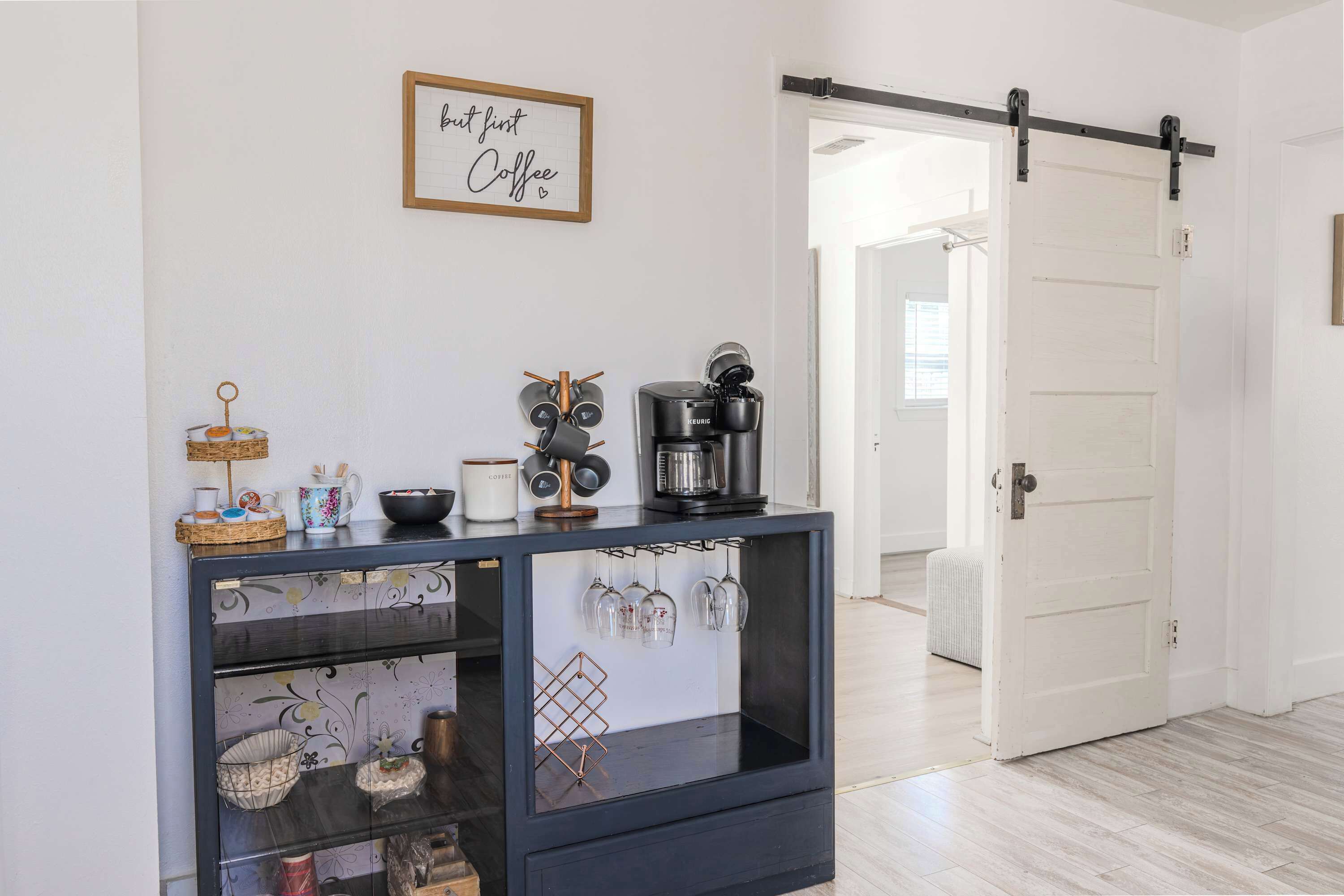 A modern kitchen with a coffee maker, a hanging wine rack, and a framed sign on the wall.