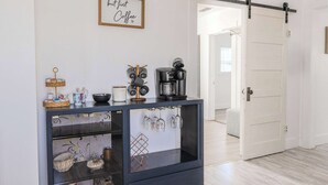 A modern kitchen with a coffee maker, a hanging wine rack, and a framed sign on the wall.
