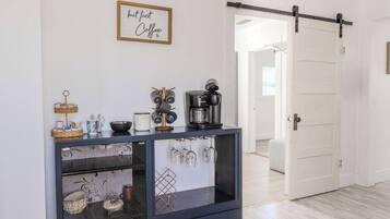 A modern kitchen with a coffee maker, a hanging wine rack, and a framed sign on the wall.
