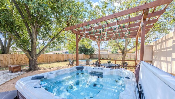 A hot tub under a wooden pergola with a wooden fence and patio furniture in the background.