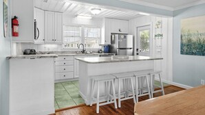A modern kitchen with white cabinetry, a central island with bar stools, a stainless steel refrigerator, and a fire extinguisher mounted on the wall. - 10% off 3-7 nights thru Oct. Pet friendly 4BR 2BA on channel. Fenced yard (North Myrtle Beach)
