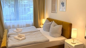 Moderni hotellihuone, jossa on suuri sänky, yöpöytä, lamppu ja kaksi kehystettyä kuvaa seinällä.