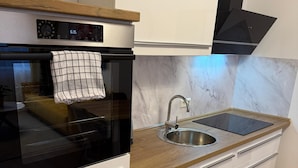 Moderni keittiö, jossa on valkoiset kaapit, musta uuni, puinen työtaso ja ruostumattomasta teräksestä valmistettu pesuallas.