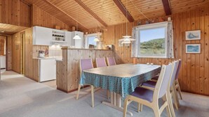 A cozy cabin interior with a wooden interior, a dining area with a table and chairs, a kitchen with white cabinets, and a large window offering a view of the outdoors.