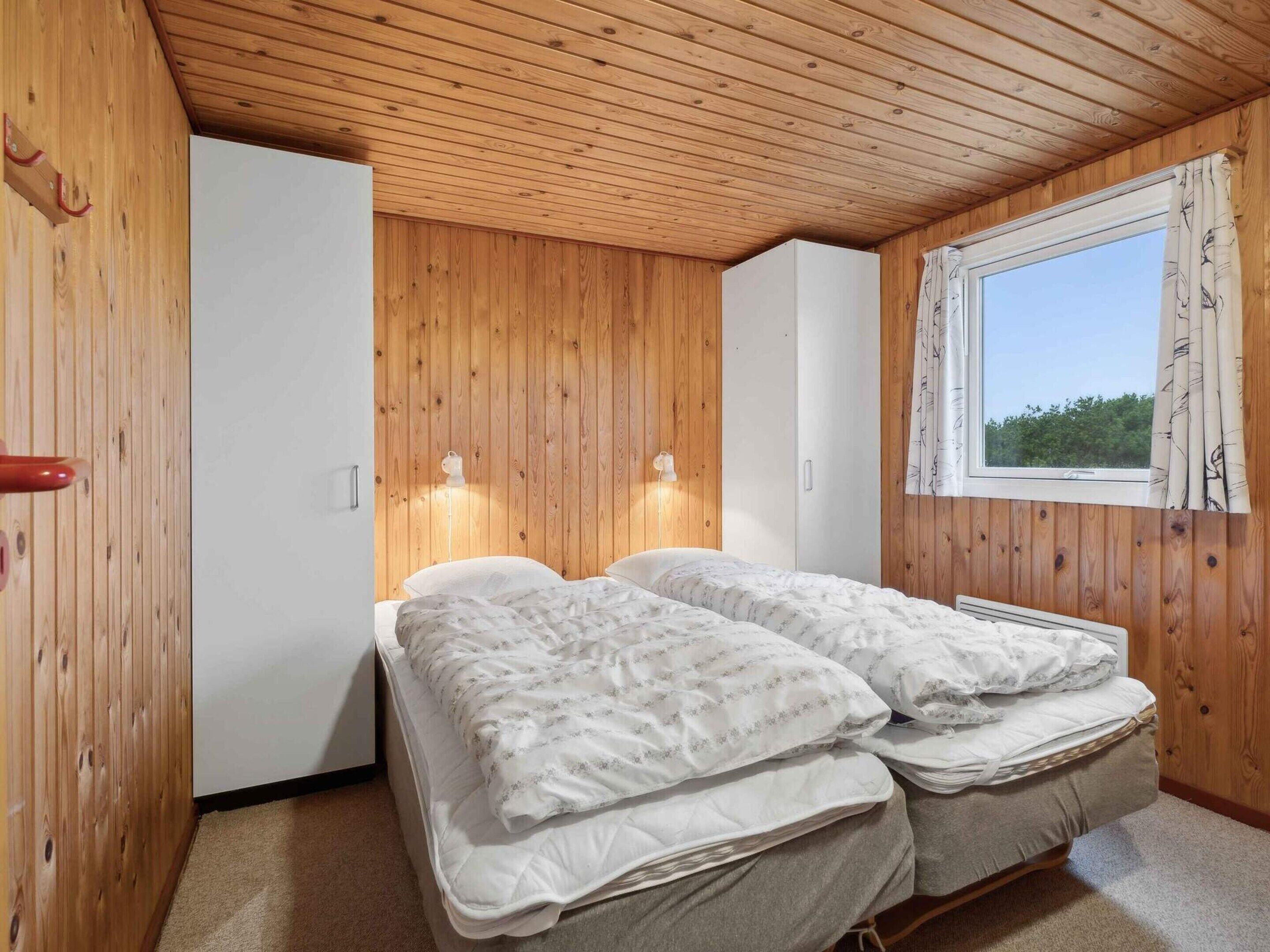 Een slaapkamer met houten wanden, een raam met gordijnen en een bed met een witte dekbed.
