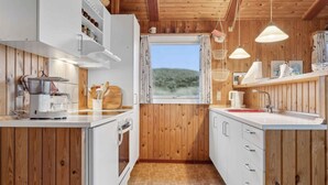 A compact kitchen with wooden walls, white cabinets, and a window overlooking a scenic view.