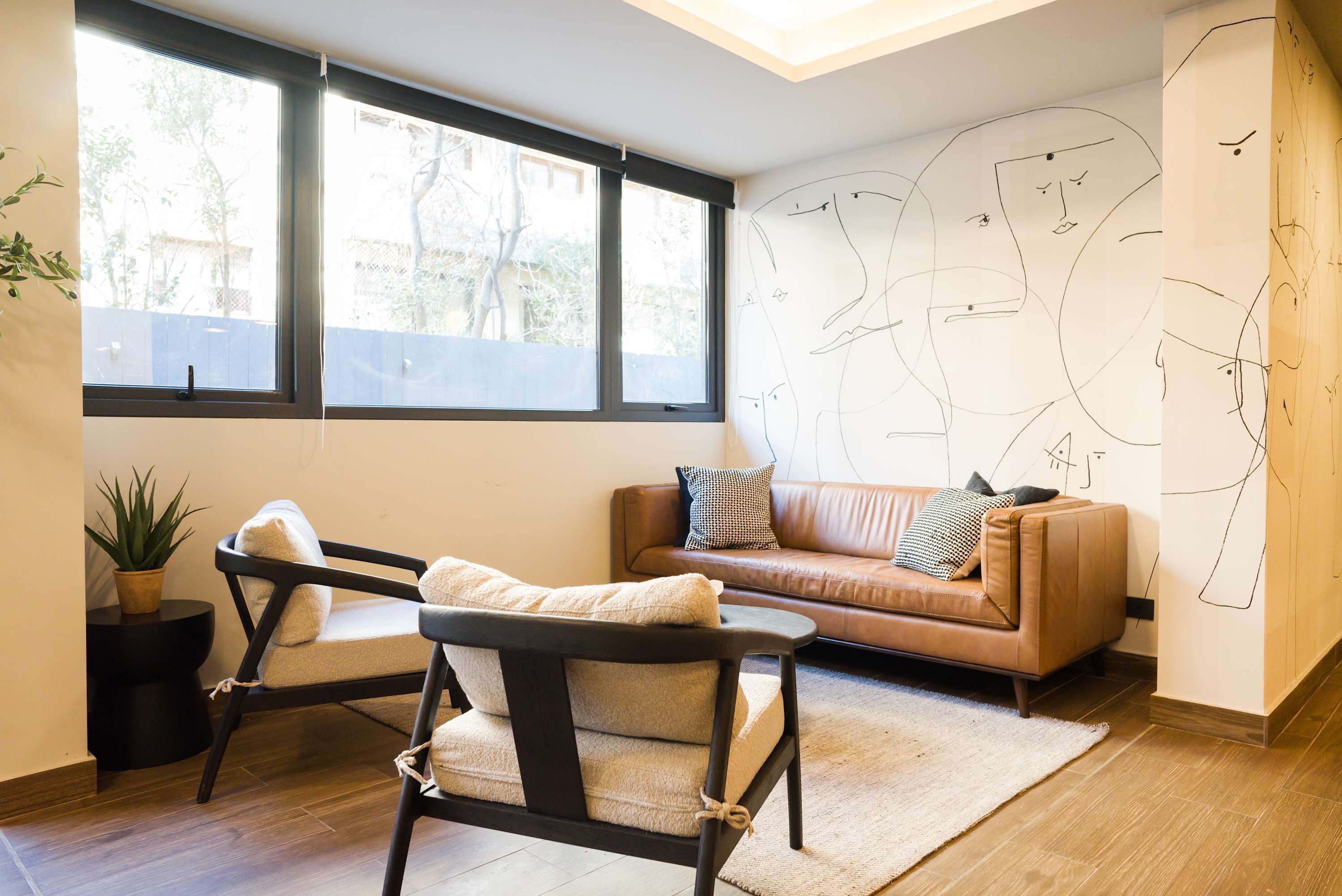 A modern living room with a brown leather sofa, a black and white armchair, and a large window with blinds.