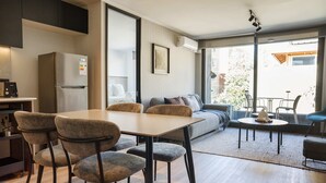 A modern living space with a dining area, kitchen, and seating by a large window. - Luxe 2BR Parkside Retreat | Pool and Gym Included (Providencia)