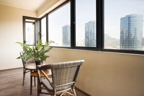 Quarto com mesa de jantar e cadeiras, planta em vaso e grandes janelas com vista para a cidade.