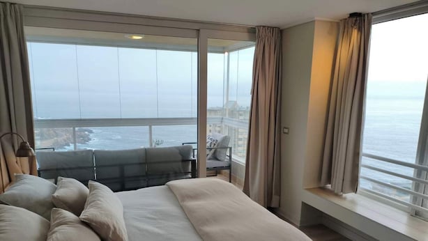 A bedroom with a large bed, a view of the sea, and a balcony with seating. - Modern 4BR Apartment with Ocean View near Concón (Valparaíso)
