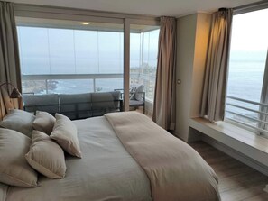 Un dormitorio con una cama grande, vista al mar y un balcón con mobiliario.