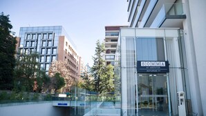 A modern building with a glass entrance and a sign reading "SOMMA by GREYSTAR ASTURIAS 77".