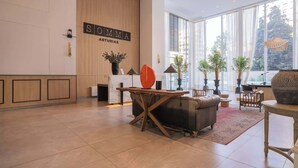 A modern hotel lobby with a reception desk, seating area, and large windows offering views of the outdoors.