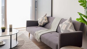 A modern living room with a grey sofa, a glass coffee table, and a large window.
