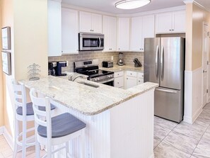 A kitchen with white cabinets, a stainless steel refrigerator, a microwave, and a granite countertop.