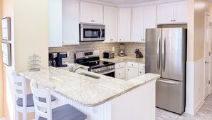 Una cocina moderna con armarios blancos, un refrigerador de acero inoxidable, un microondas integrado y una encimera de granito.
