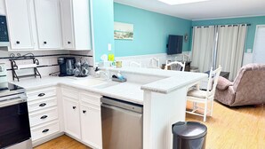 A modern kitchen with white cabinetry, a granite countertop, and a built-in dishwasher. - Experience Tilghman Beach & Racquet 364! Second Row, Pools, Tennis, Close to Main Street! (North Myrtle Beach)