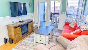 A living room with a TV, wooden cabinet, white dresser, red sofa, and a view of the outside balcony. - Experience Tilghman Beach & Racquet 364! Second Row, Pools, Tennis, Close to Main Street! (North Myrtle Beach)