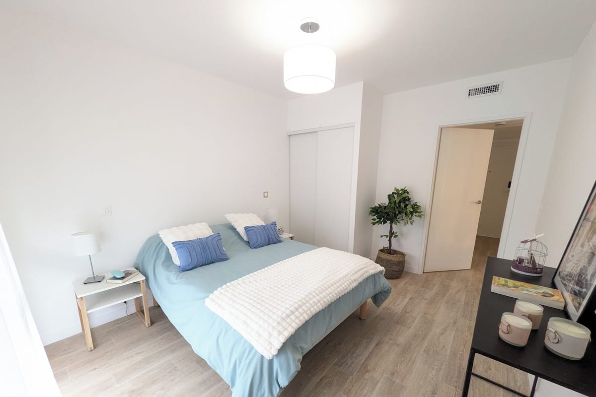 Une chambre à coucher avec un lit, une table de chevet, une lampe, une plante en pot et une porte.