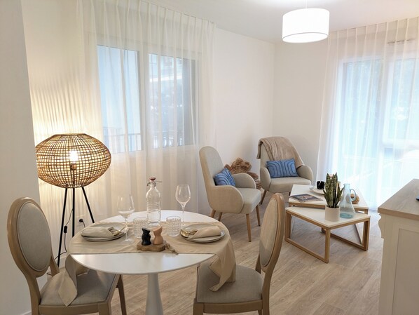 A modern living room with a round dining table, two armchairs, a sofa, and a coffee table. There are curtains on the windows, a floor lamp, and a potted plant on the coffee table. - Résidence de Nogent sur Marne (Nogent-sur-Marne)