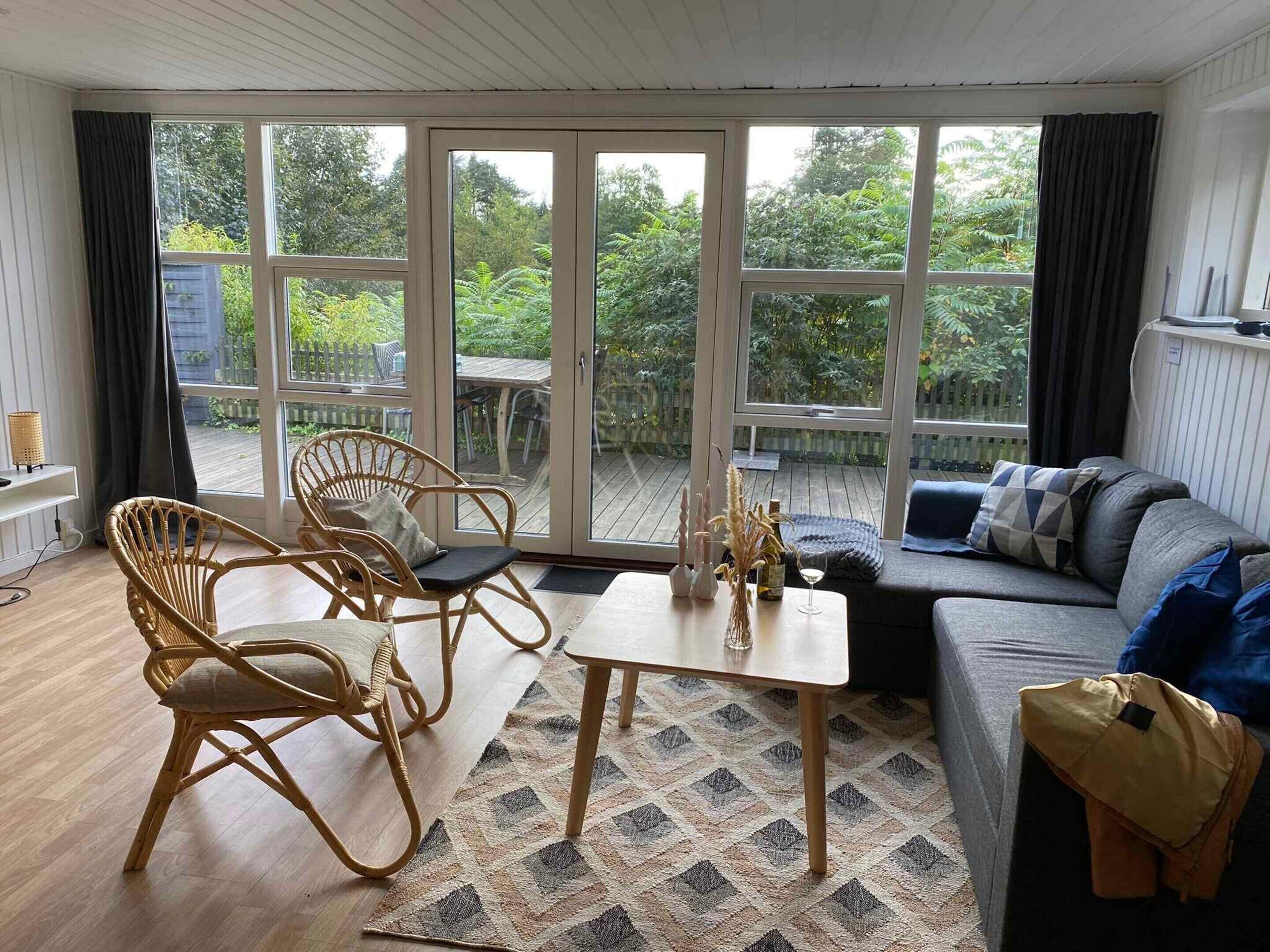 Un vaste salon doté d’une grande porte-fenêtre coulissante donnant sur une terrasse aménagée avec un canapé, des fauteuils et une table basse.