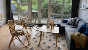 A spacious living room with a large sliding glass door leading to a deck, furnished with a sofa, chairs, and a coffee table. - 5 Star Holiday Home in Ebeltoft (Ebeltoft)
