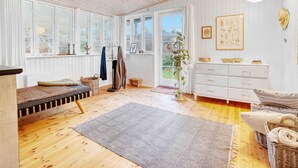 Una stanza accogliente con parquet, una panca, una cassettiera bianca e un'ampia finestra con tende.
