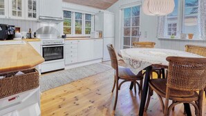 Una cucina moderna con mobili bianchi, soffitto in legno e zona pranzo con sedie in vimini e un tavolo.