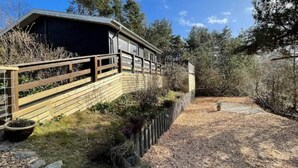 Eine rustikale Holzhütte mit einer Holzterrasse und einem umzäunten Garten.