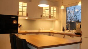 Eine moderne Küche mit weißen Schränken, einer Holzauskładung, Pendelleuchten und einem Fenster mit Blick auf Bäume.