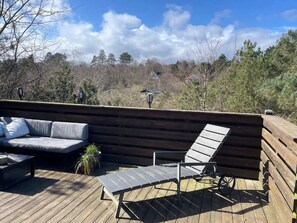 A wooden deck with a sofa and two lounge chairs.
