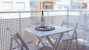 A balcony with a white table and chairs, a bottle of wine, and two glasses.