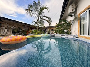 A swimming pool with inflatable rings, surrounded by palm trees and a building with a tiled exterior. - Boem - High (Yaoundé)