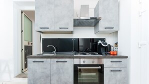 Een compacte keuken met een ingebouwde oven, een gasfornuis en een roestvrijstalen afzuigkap.