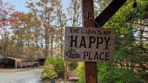 A wooden sign with the text "The cabin is my happy place" mounted on a wooden post.