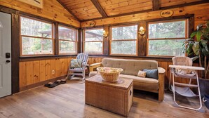 A cozy cabin interior with a wooden floor, a sofa, a chair, a basket, and a cat tree.