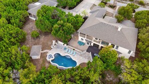 An aerial view of a two-story house with a swimming pool, surrounded by dense greenery. - Grand Lakehouse Estate with Infinity Pool & Views (Austin)