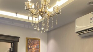 A living room with a green sofa, a chandelier, an air conditioner, and a painting on the wall. - Gardenia Park Al Rawabi Serviced Apartments Economy (Jeddah)