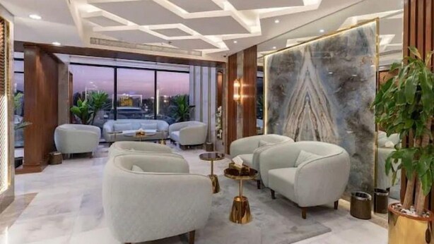 A modern living room with a large window, two sofas, a coffee table, and a marble wall. - Gardenia Park Al Rawabi Serviced Apartments Economy (Jeddah)