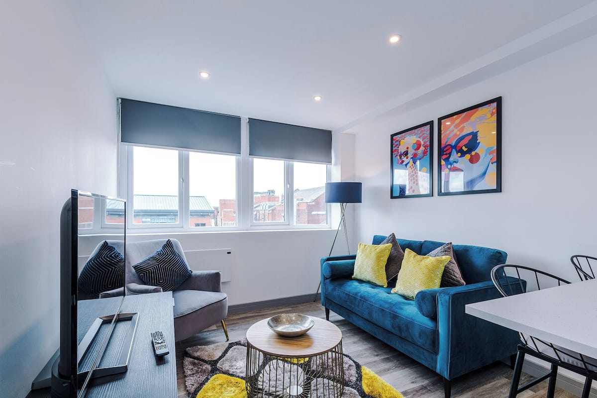 A modern living room with a blue sofa, a coffee table, a TV, and artwork on the wall.