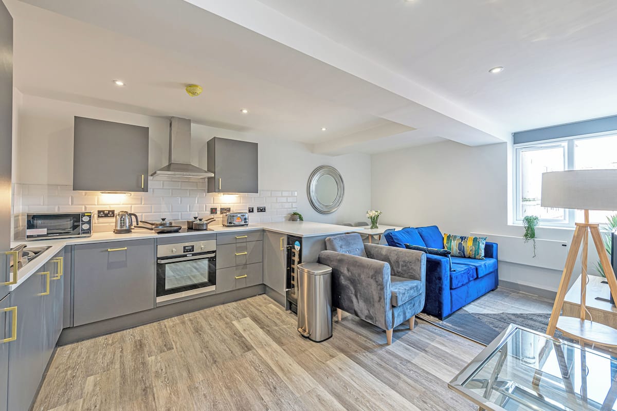 A modern kitchen with grey cabinets, a built-in oven, and a stainless steel trash bin.