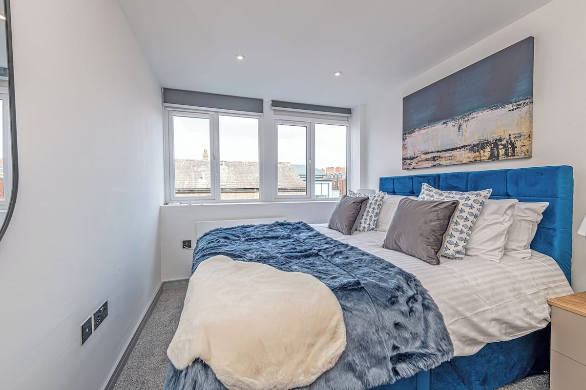 A modern bedroom with a large bed, a view of the city, and a painting on the wall.