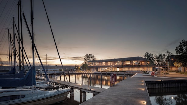 A marina with boats docked, a wooden pier, and a modern building with large windows.