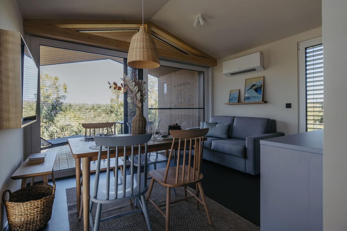 Una sala de estar moderna con comedor, ventanas amplias y un sofá gris.